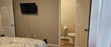 Een slaapkamer met een bed, een aan de muur bevestigde televisie en een open deur naar een badkamer.