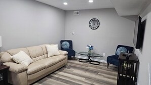 A living room with a beige sofa, two armchairs, a glass coffee table, and a wall clock. - Family-Friendly 4BR Home in Elkton - AC, High-Speed WiFi & Relaxing Vibes (Elkton)