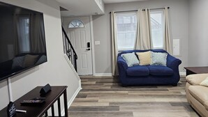 A modern living room with a blue sofa, a beige sofa, a TV, and a wooden floor. - Family-Friendly 4BR Home in Elkton - AC, High-Speed WiFi & Relaxing Vibes (Elkton)