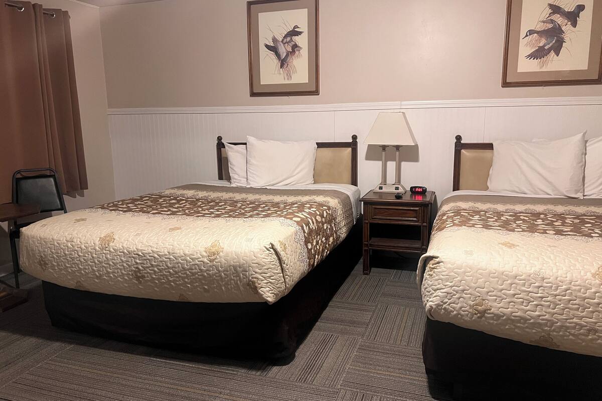 A hotel room with two beds, a nightstand with a lamp, and two framed pictures on the wall.