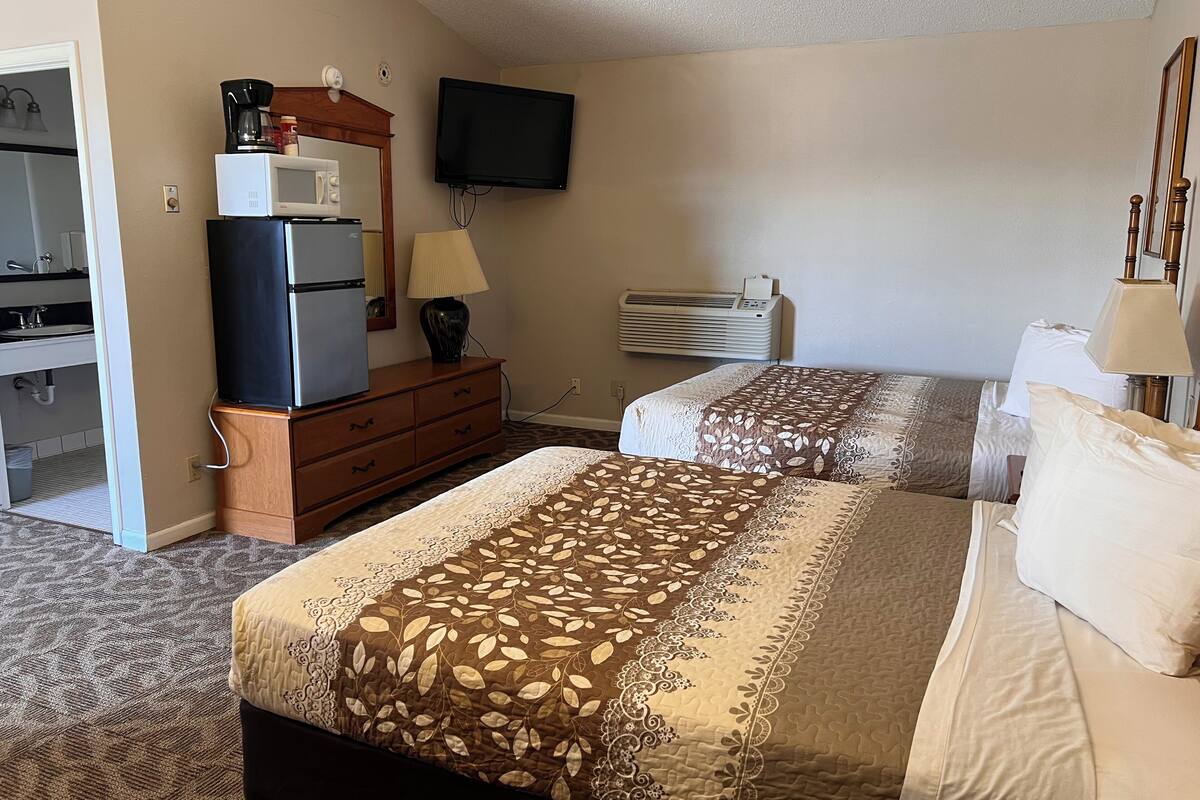 A hotel room with two beds, a refrigerator, a microwave, a television, and an air conditioning unit.