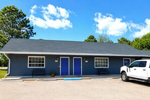 A single-story building with a dark blue exterior, two blue doors, and a white vehicle parked in front. - Dew Drop Inn Motel by OYO Miller SD (Miller)
