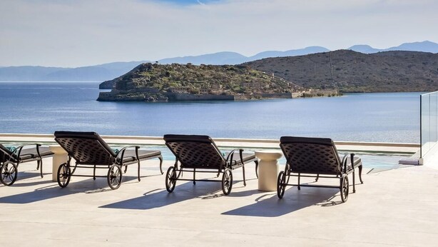 Une terrasse avec des chaises longues donnant sur une étendue d’eau et une île lointaine.