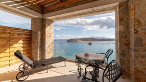 Un balcon avec un mur en pierre, une clôture en bois à lattes, une table avec des chaises et un fauteuil de relaxation.