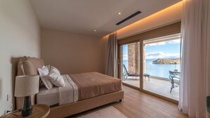 Une chambre à coucher comprenant un lit, une table de chevet, une lampe, une vue sur la mer et un balcon avec des meubles d’extérieur.