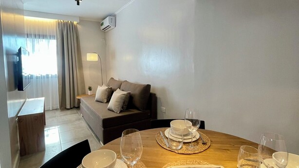 Un comedor moderno con una mesa redonda preparada para dos personas, un sofá al fondo y una lámpara colgante grande.