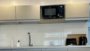 Una cocina moderna con microondas, cafetera y una mesa de comedor preparada para cuatro personas, con copas de vino y platos.
