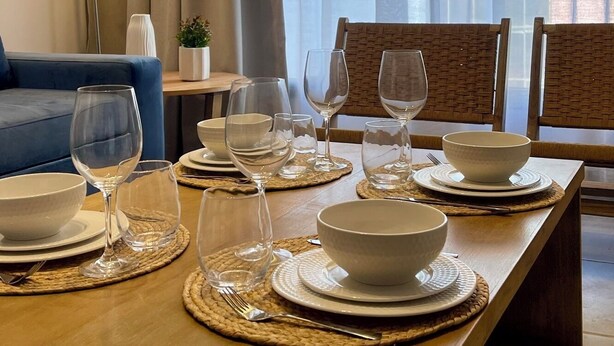 A dining area with a wooden table set for four, including plates, bowls, and wine glasses. There is a blue sofa and a lamp in the background. -  Park Apartment by Vilvey Turismo (Mendoza)