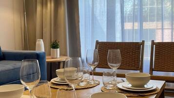 A dining area with a wooden table set for four, including plates, bowls, and wine glasses. There is a blue sofa and a lamp in the background.