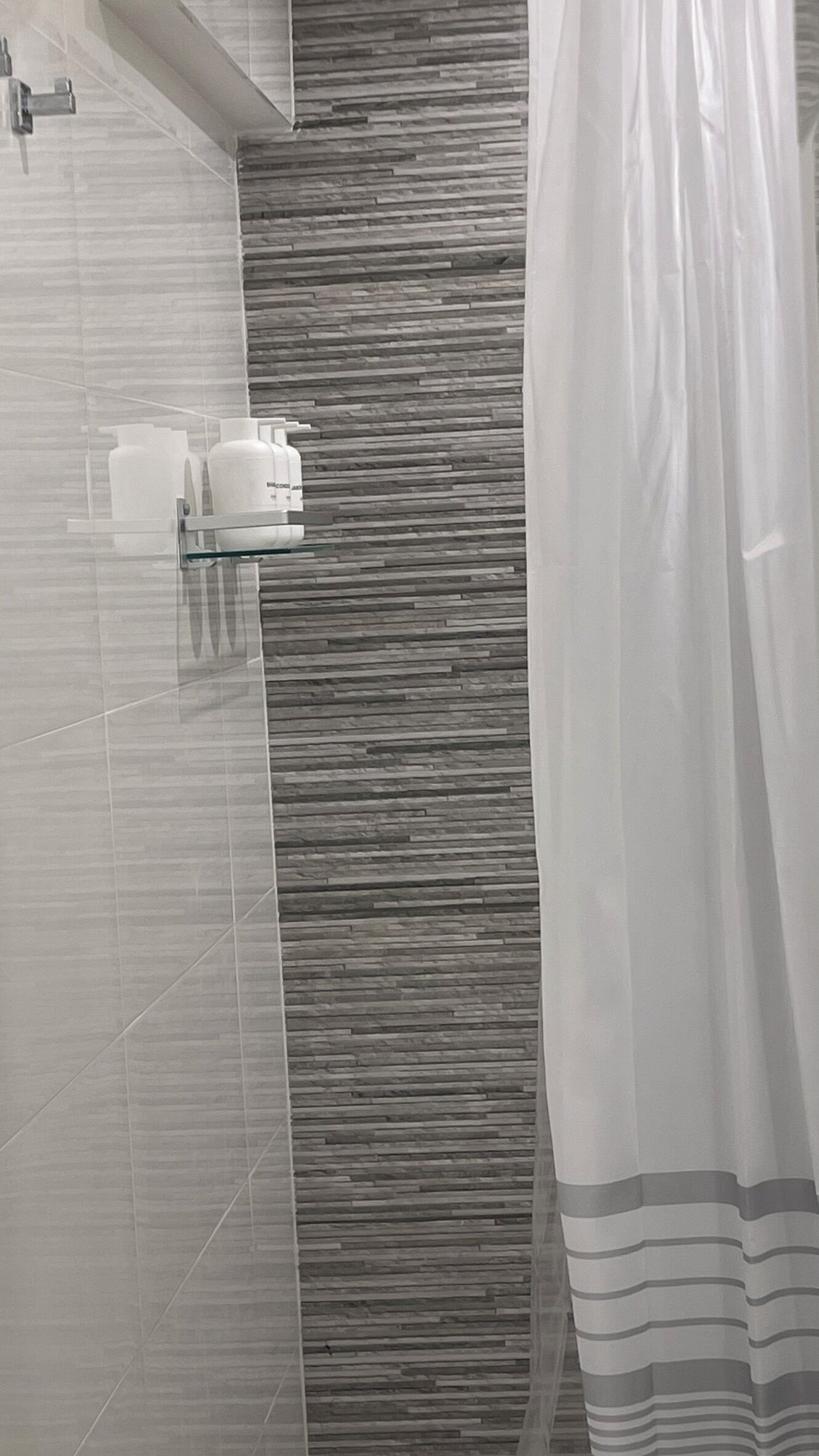 A bathroom with a tiled wall, a shower curtain, and a shelf with toiletries.