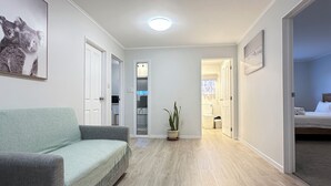 Une pièce spacieuse avec un canapé gris, un plancher en bois, un luminaire au plafond et une porte donnant sur une autre pièce.
