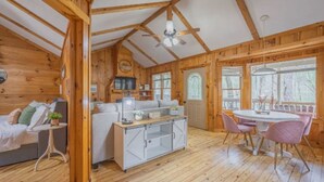 A cozy cabin interior with a wooden interior, a kitchenette, a dining area, and a bedroom with a bed and a small table. - Up Country, Creekside/Hot Tub (Dahlonega)