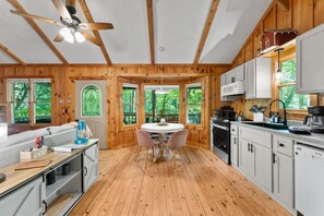 A cabin with a wooden interior, a dining area, kitchen, and large windows. - Up Country, Creekside/Hot Tub (Dahlonega)