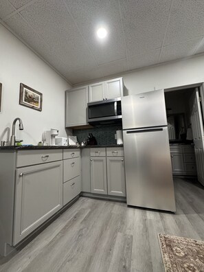 A modern kitchen with grey cabinets, a stainless steel refrigerator, a microwave, and a sink.