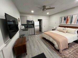 A compact bedroom with a bed, a desk, and a kitchenette.