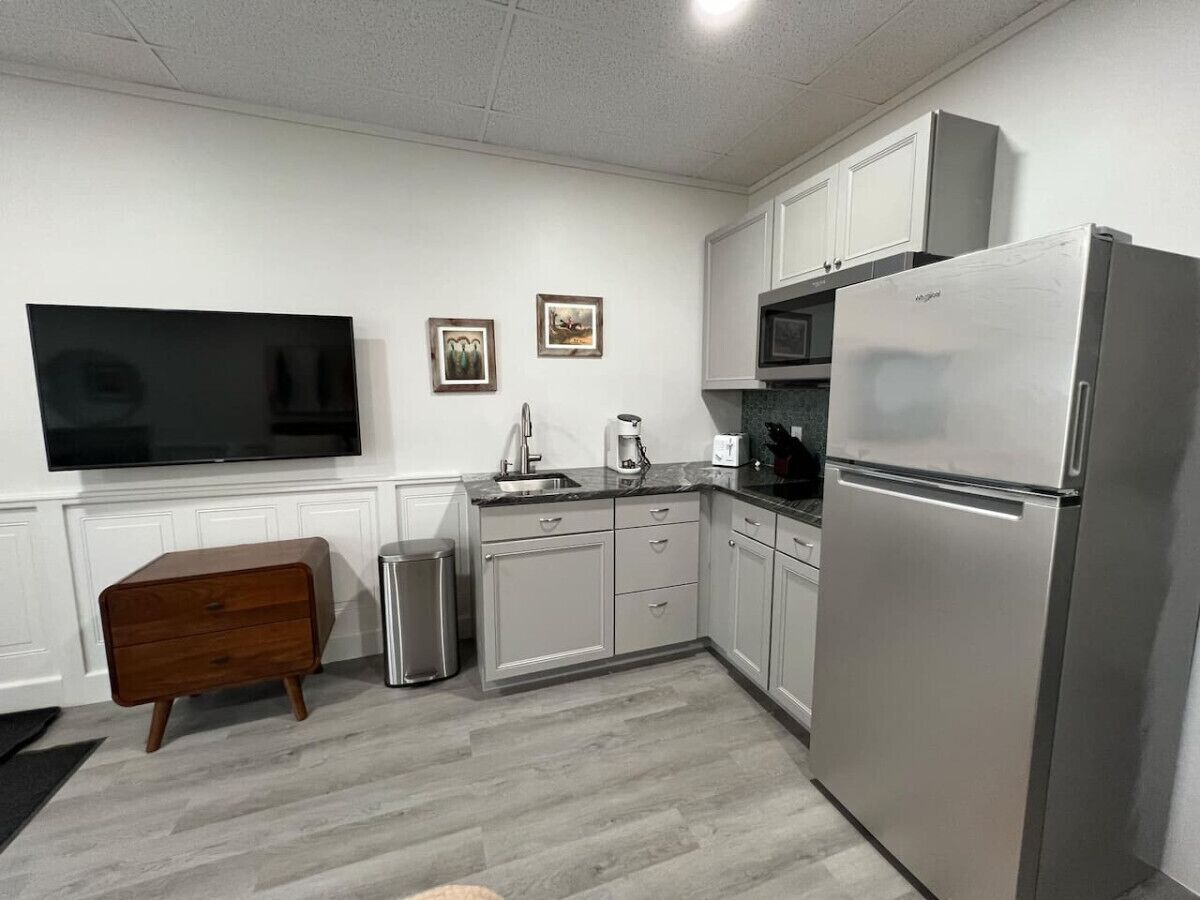 A compact kitchen with a stainless steel refrigerator, a microwave, a sink, and a wooden cabinet.