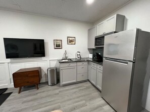 A compact kitchen with a stainless steel refrigerator, a microwave, a sink, and a wooden cabinet. - Charming Studio Apartment - Cozy & Convenient! (Fort Fairfield)