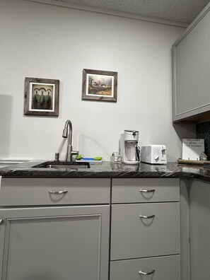 Eine Küche mit Spüle, Kaffeemaschine und Toaster. An der Wand hängen zwei Bilder in Rahmen.