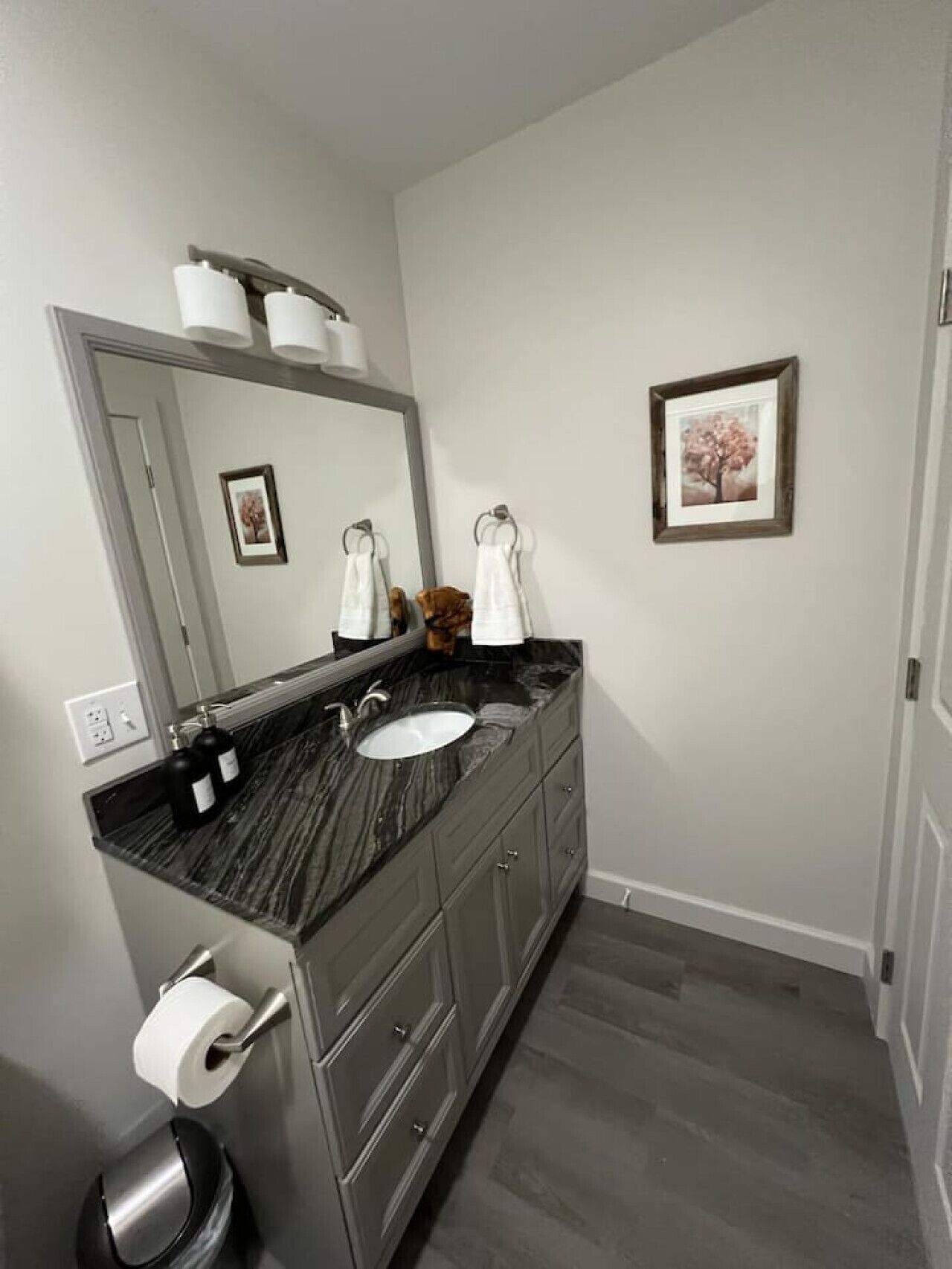 Un baño con un lavabo de mármol oscuro, un espejo grande y un cuadro en la pared.