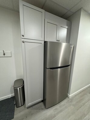 A kitchen with white cabinets, a stainless steel refrigerator, and a trash can.