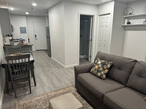 A modern living room with a gray sofa, a patterned throw pillow, and a wooden dining table with chairs.