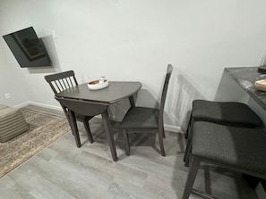 A dining area with a table and four chairs, a small rug, and a television mounted on the wall.