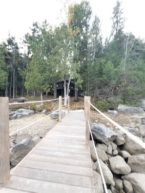Un puente de madera que lleva a un edificio rodeado de árboles y rocas.