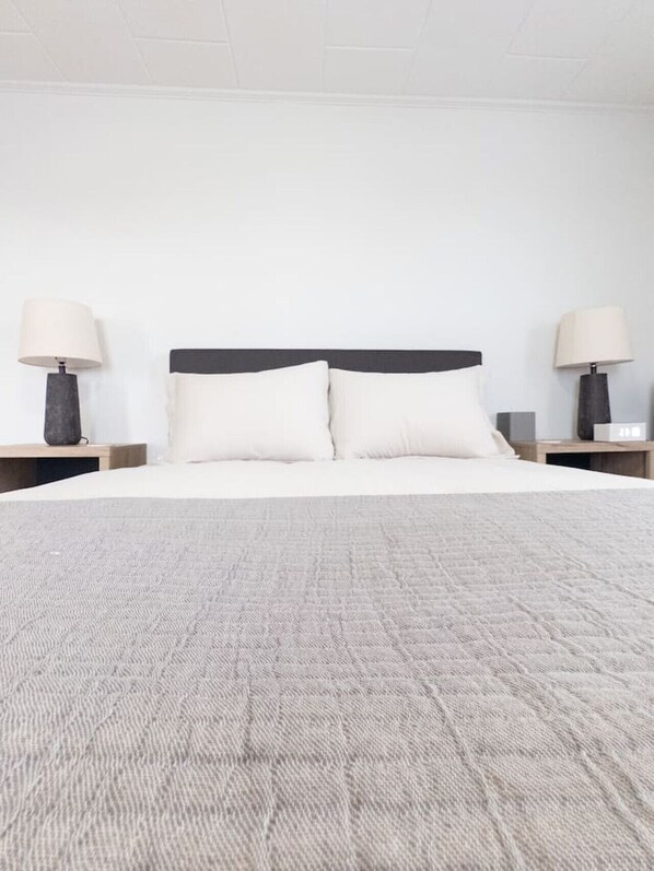 A neatly made bed with a grey textured blanket, two bedside tables with lamps, and a plain white wall.