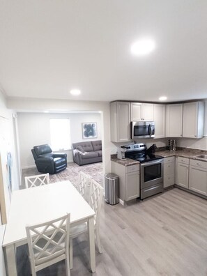 A compact kitchen with white cabinets, a microwave, stove, and a trash can.