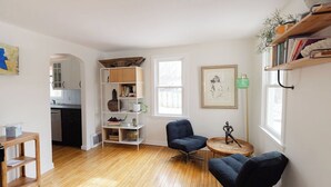 Una sala de estar con piso de madera, una estantería, dos sillones, una mesa redonda y un ventanal.