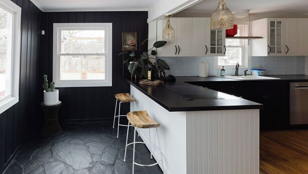 Una cocina moderna con una paleta de colores blanco y negro, que incluye una isla grande con taburetes, suelo de piedra e iluminación colgante.