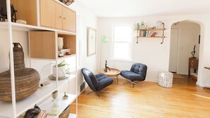 Un salón amplio con suelo de madera, una estantería, dos sillones y una mesa de centro redonda.