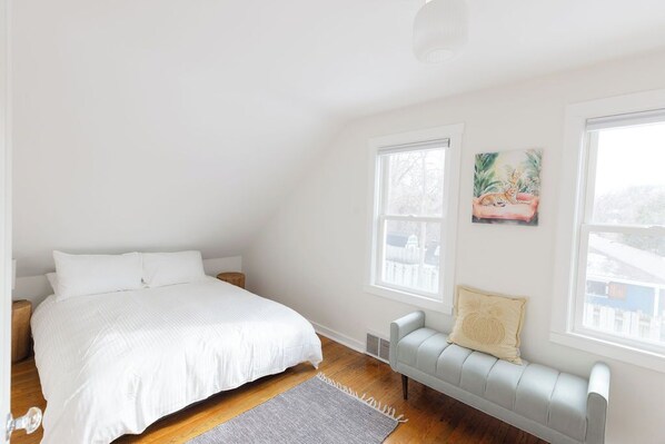 Un dormitorio con cama, un banco y dos ventanas.