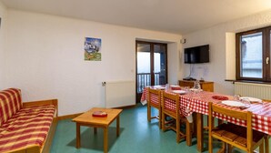 A furnished room with a sofa, a dining table set with a red and white checkered tablecloth, and a television mounted on the wall.
