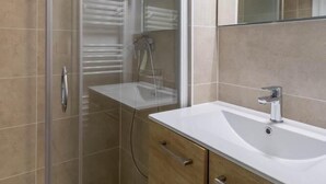 A modern bathroom with a glass shower enclosure, a white sink, and wooden cabinetry.