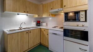 A compact kitchen with wooden cabinets, a white sink, a coffee maker, a toaster, a dishwasher, and a stove with an oven.