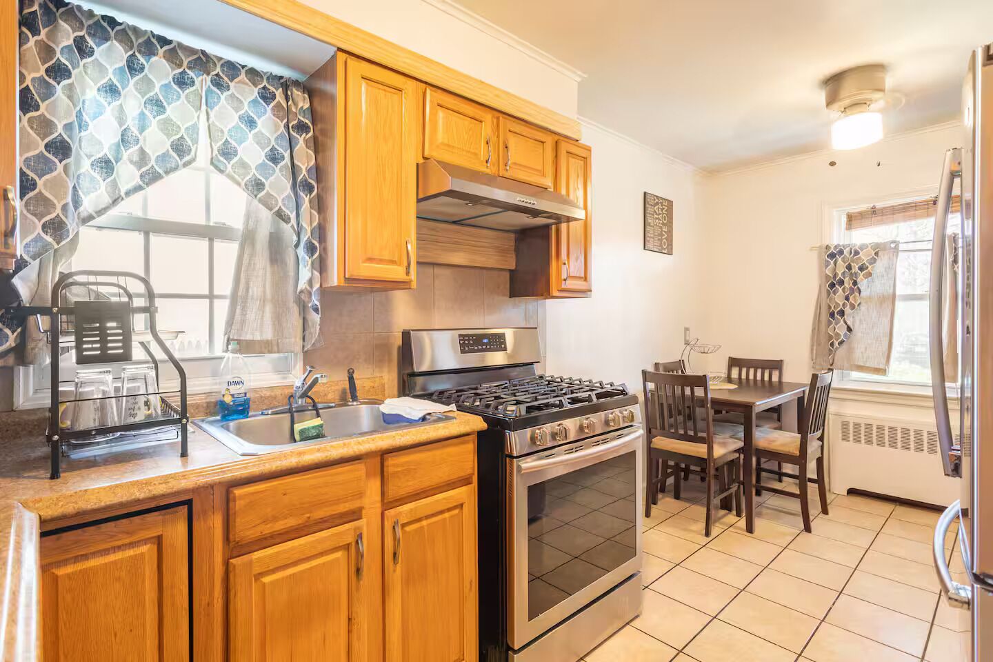 A kitchen with wooden cabinets, a stainless steel stove, and a dining area with a table and chairs.