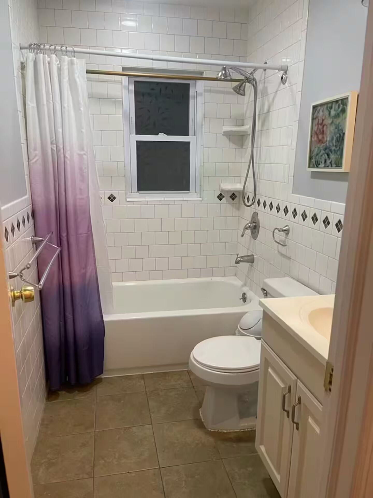 Une salle de bain équipée d’une baignoire, de toilettes et d’un lavabo, avec des carreaux blancs et une fenêtre.