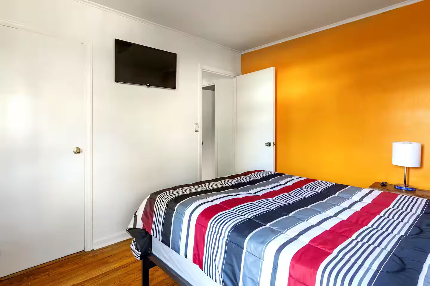 Un dormitorio con cama, televisor en la pared y puerta que da a otra habitación.