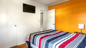 Un dormitorio con cama, televisor en la pared y puerta que da a otra habitación.