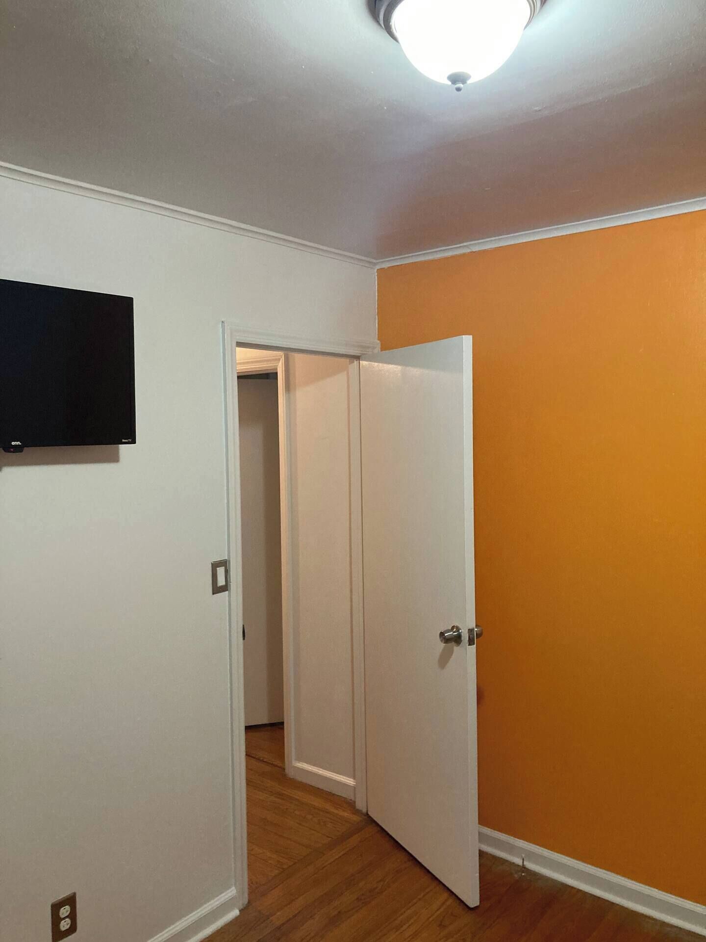 A room with a white door, an orange wall, and a ceiling light.