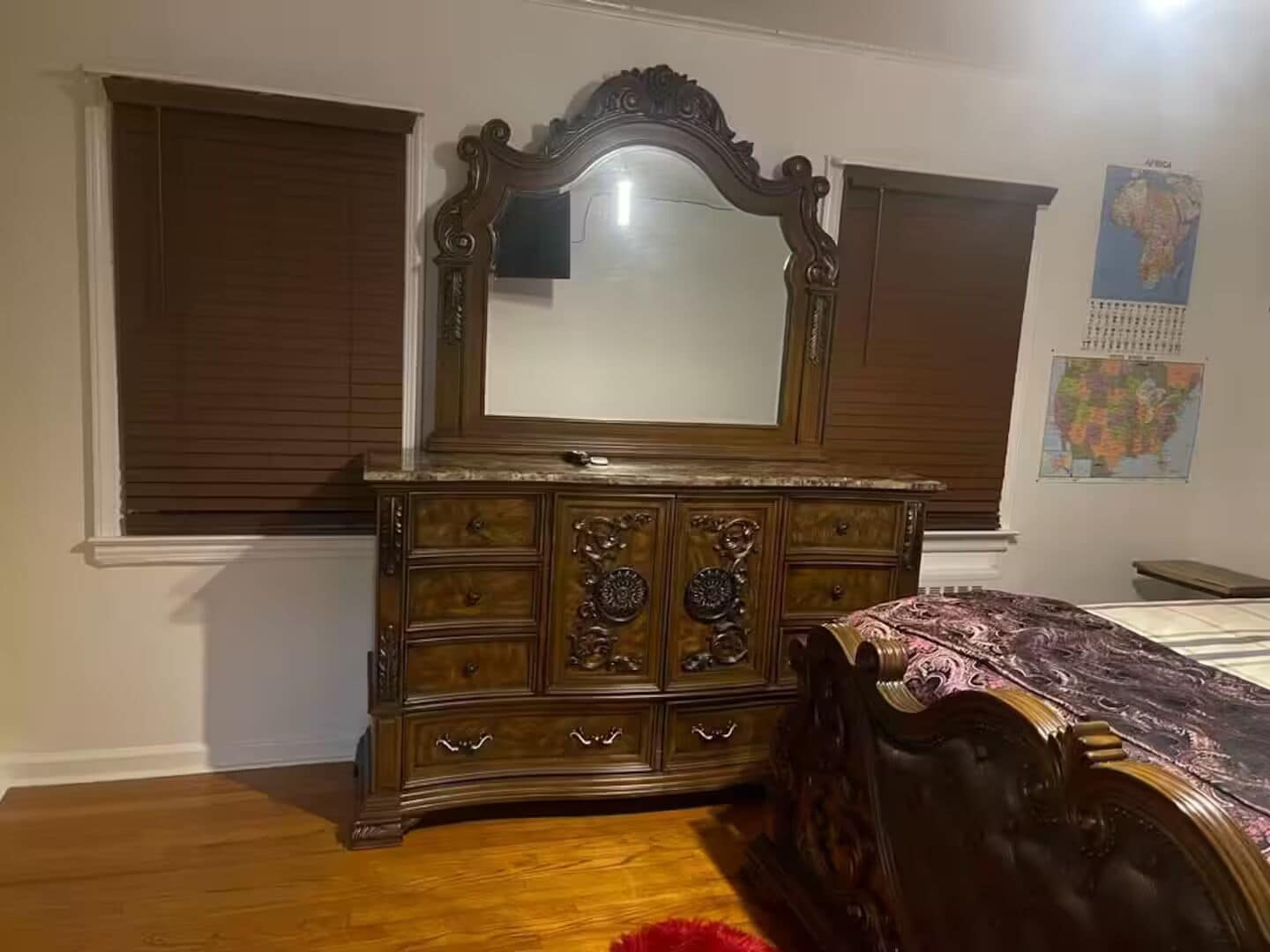 A bedroom with a wooden dresser, a large mirror, and a bed with a patterned bedspread.