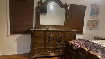 A bedroom with a wooden dresser, a large mirror, and a bed with a patterned bedspread.