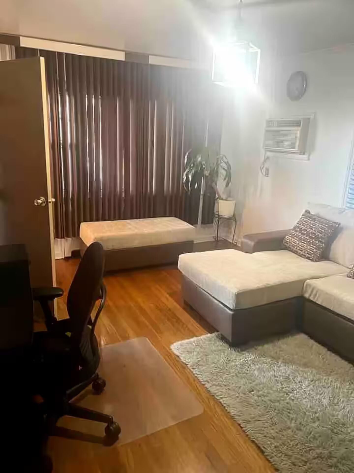A living room with a sofa, a chair, a small table, a plant, and a window with curtains.