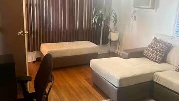 A living room with a sofa, a chair, a small table, a plant, and a window with curtains.
