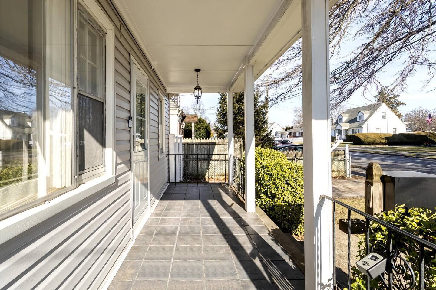 A covered porch with a tiled floor, a metal gate, and a hedge.