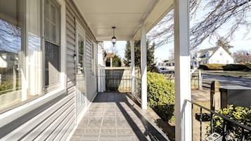 A covered porch with a tiled floor, a metal gate, and a hedge.
