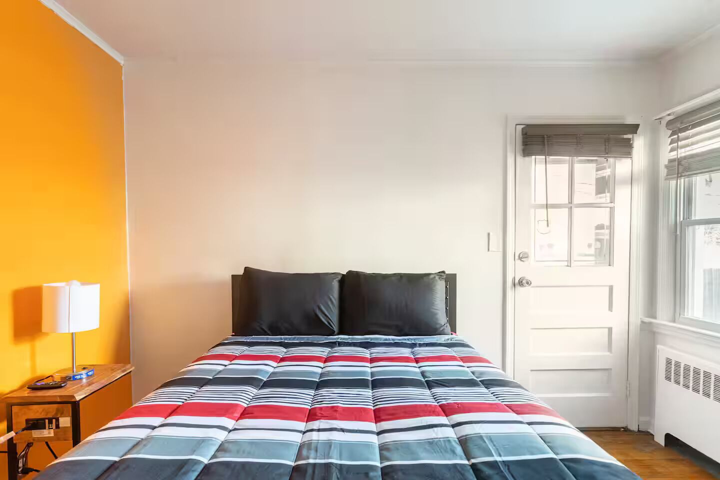 A bed with a striped comforter, a bedside lamp, and a door with a window.