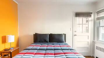 A bed with a striped comforter, a bedside lamp, and a door with a window.