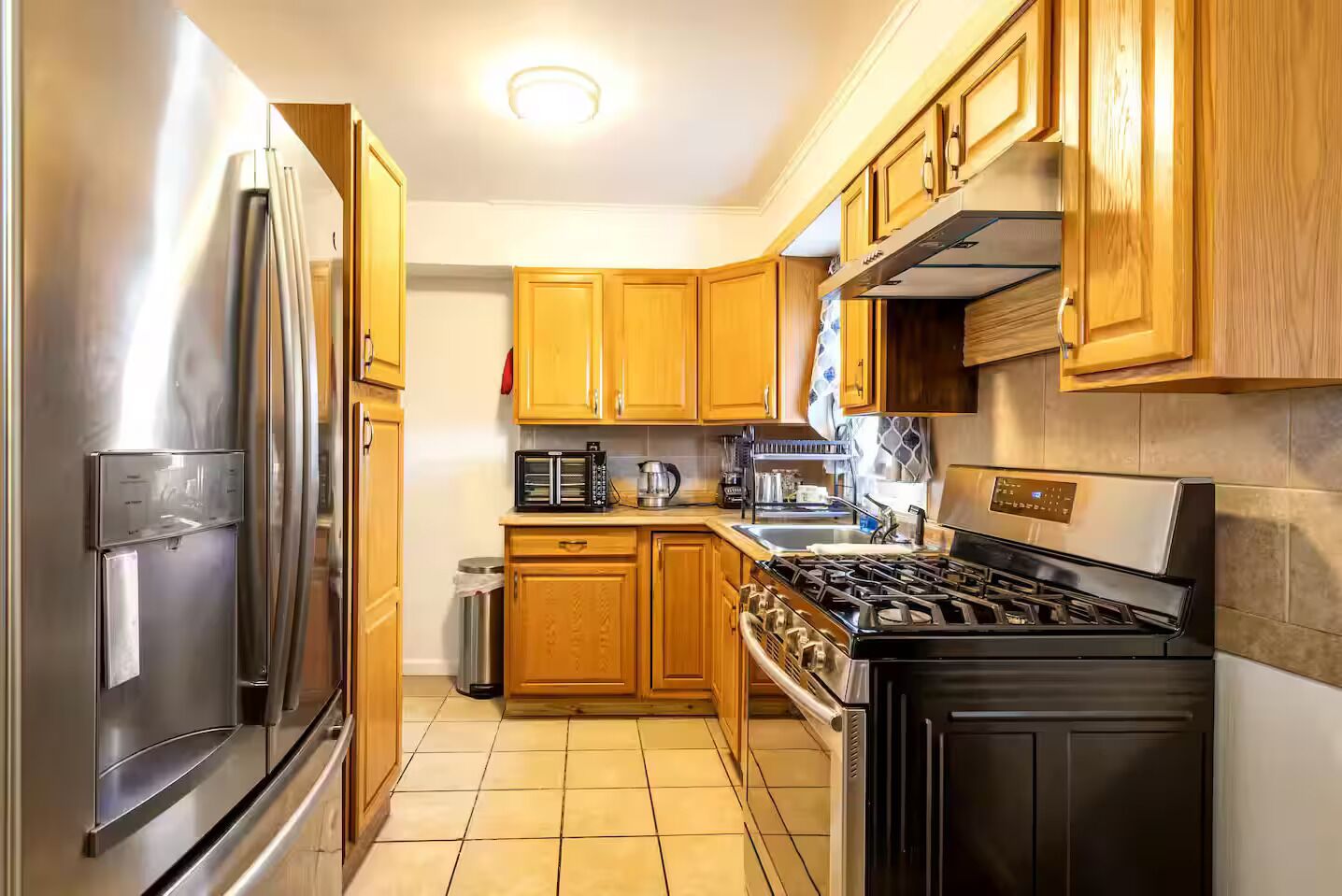 Una cocina con armarios de madera, un refrigerador de acero inoxidable, un microondas, una estufa y un lavamanos.